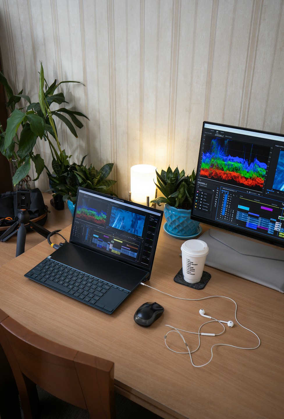 Laptop und Monitor mit Bearbeitungssoftware auf einem Holztisch.